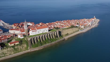 Aerial-of-scenic-Church-of-Saint-George-standing-on-hill-in-coastal-town-Piran,-Slovenia