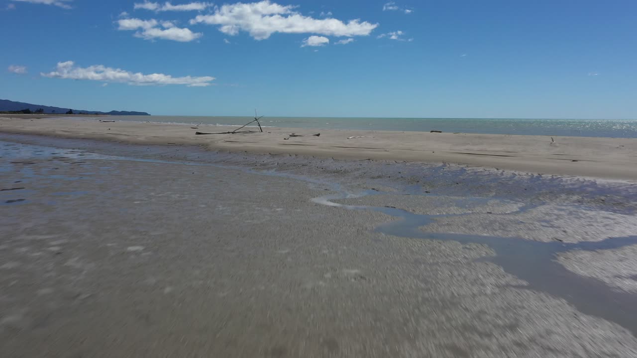 Drone flys towards sandbar with beautiful blue sky in background on a sunny summer's day