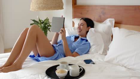 relaxing in bed, woman in pajamas enjoying tablet with coffee nearby, at home