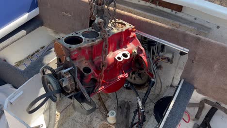 an onboard 4 cylinder engine block is slowly lifted from a boat with a chain and hoist