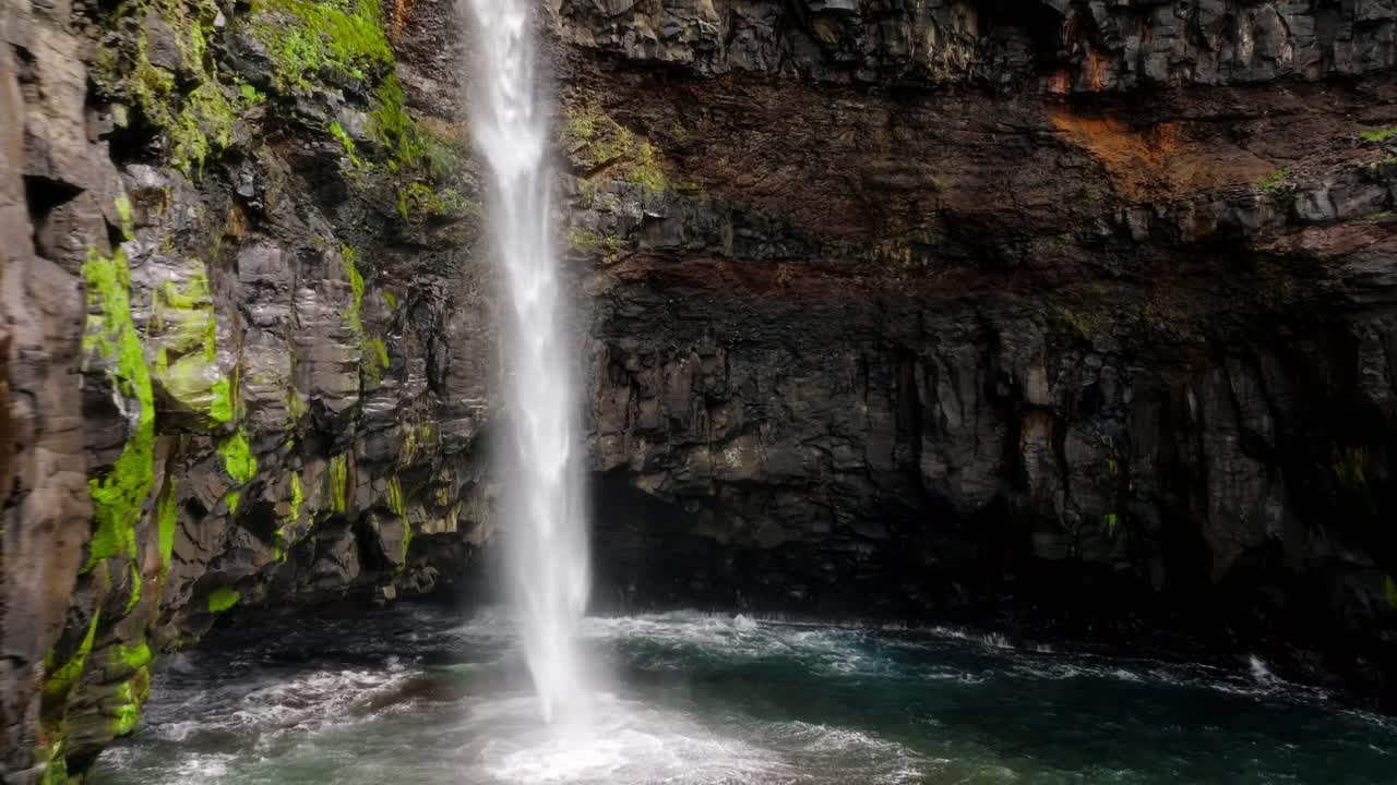 A stunning vertical waterfall plunges into the ocean amid rocky cliffs in Faroe Islands