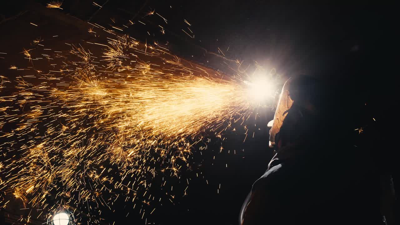 un primer plano de un hombre soldando metal en una habitación oscura con chispas volando por todas partes