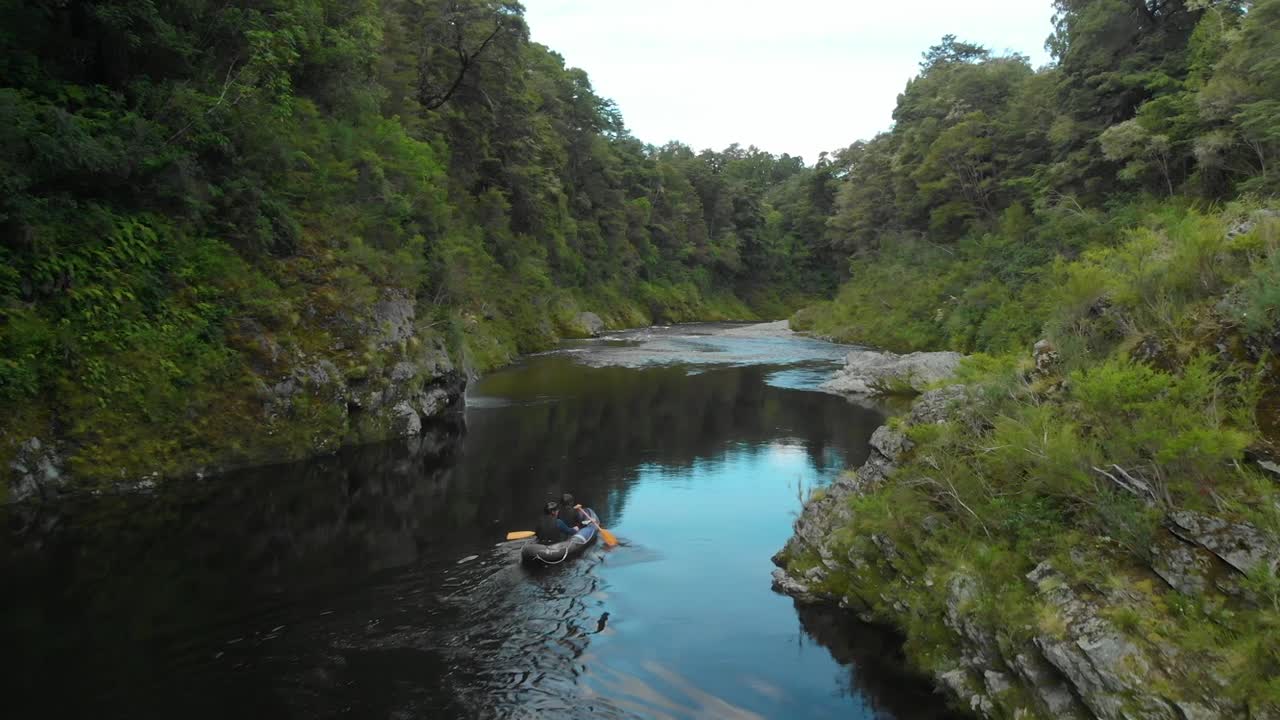 cámara lenta - dos machos reman en canoa a través de un cañón rocoso en el río pelorus, nueva zelanda con rocas y bosque en el fondo - drone aéreo