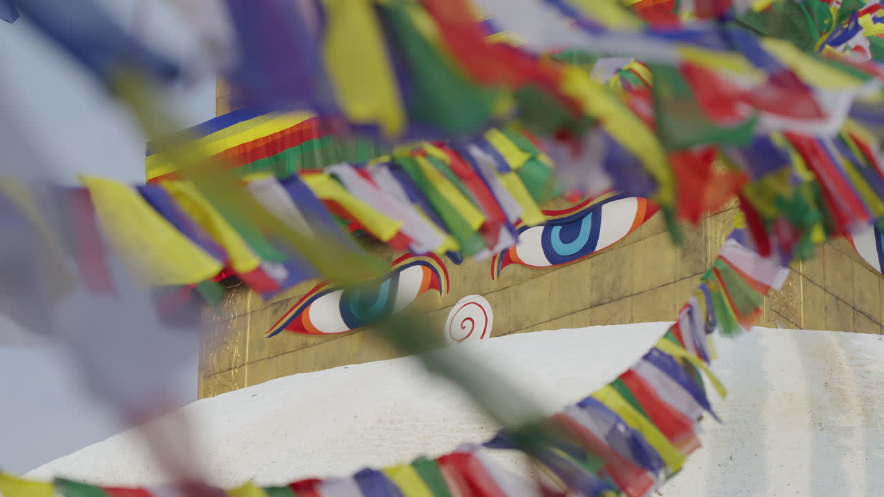 Buddhist prayer flags flutter gently over the Buddha’s eyes at Boudhanath Stupa, Nepal. The wind carries peace and calm energy, symbolizing freedom, faith, and spiritual harmony