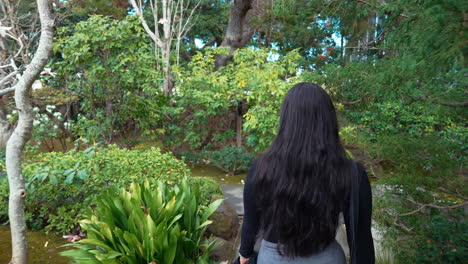 a 4k slow-motion, stabilized video depicting a beautiful young middle eastern female model exploring a lush japanese tea garden walking along a garden path, peninsula, california