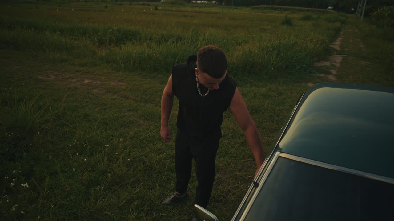 Man getting into a vintage car in a field at sunset