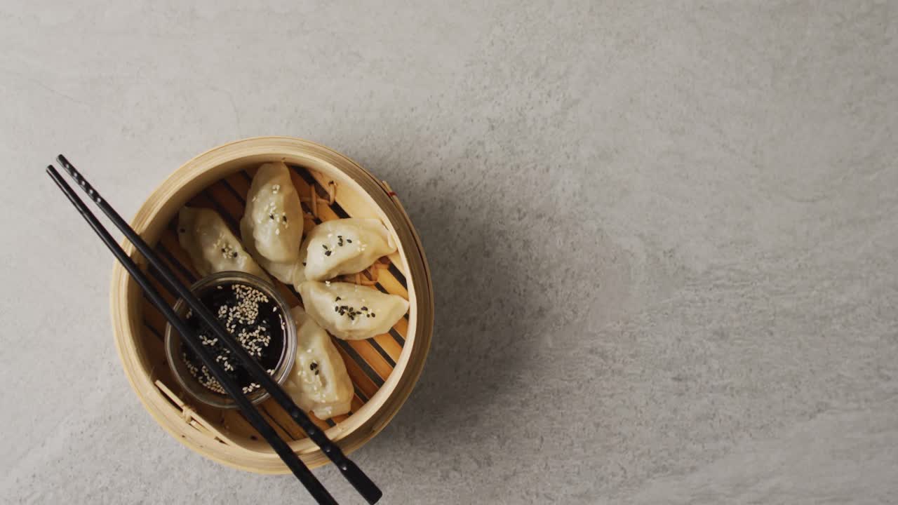 Composition of bamboo steamer with gyoza dumplings and chopsticks with soy sauce on grey background