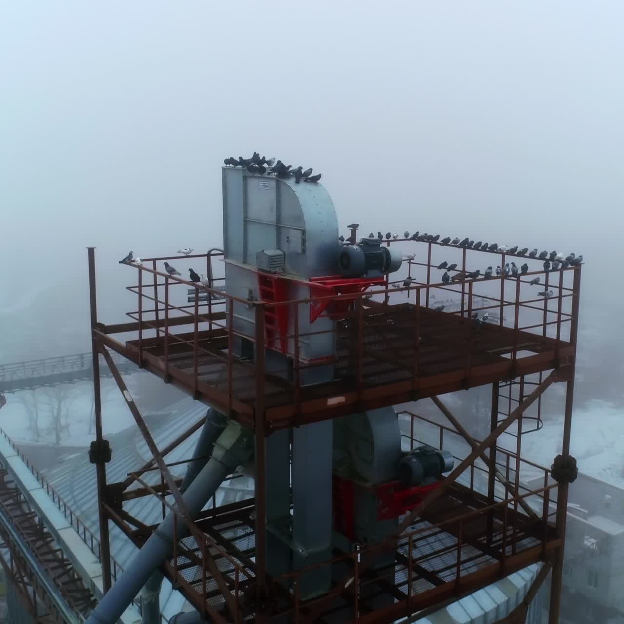 High metal construction towering over the elevator tanks. Modern agricultural silo plant with different premises. Misty weather background