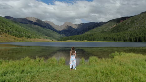 aerial cinematic drone circling female women model actress cute dress walking toward piney lake ranch vail beaver creek colorado gore range mountain landscape windy breeze summer rain sun clouds calm