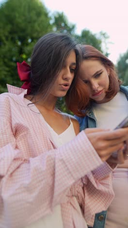 two young women looking at a smartphone in a park