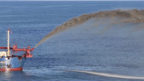 Aerial view of a dredger pumping sand into the ocean, under clear skies, showcasing industrial maritime activity