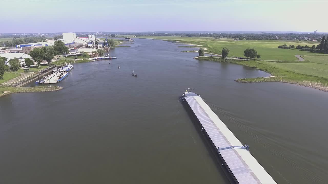 A drone shot panning backwards, flying over a river while revealing a big cargo ship in the Netherlands