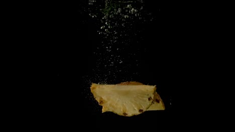 dos jugosas rebanadas de piña cayendo juntas en el agua oscura y clara