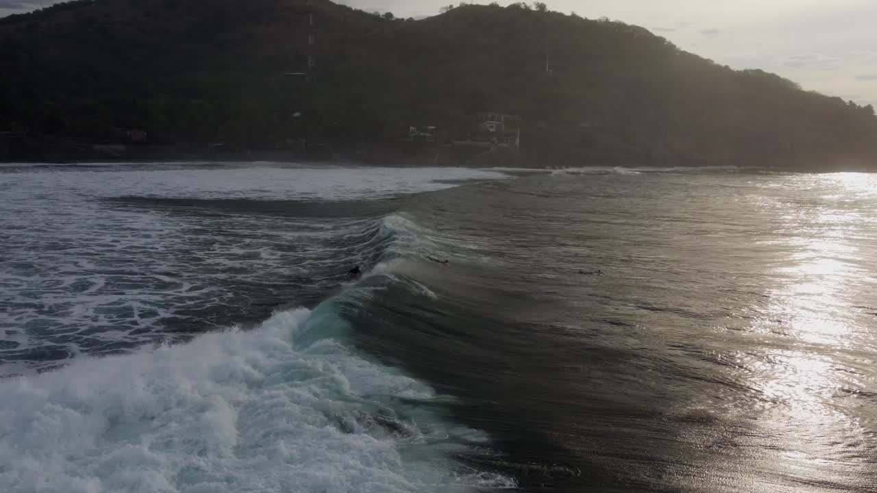 Surfer rides big, pushy shore break surf wave in golden dusk lighting
