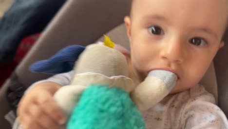 bebé lindo con un juguete en la boca, balanceando su silla hacia atrás y adelante, agarra la cámara