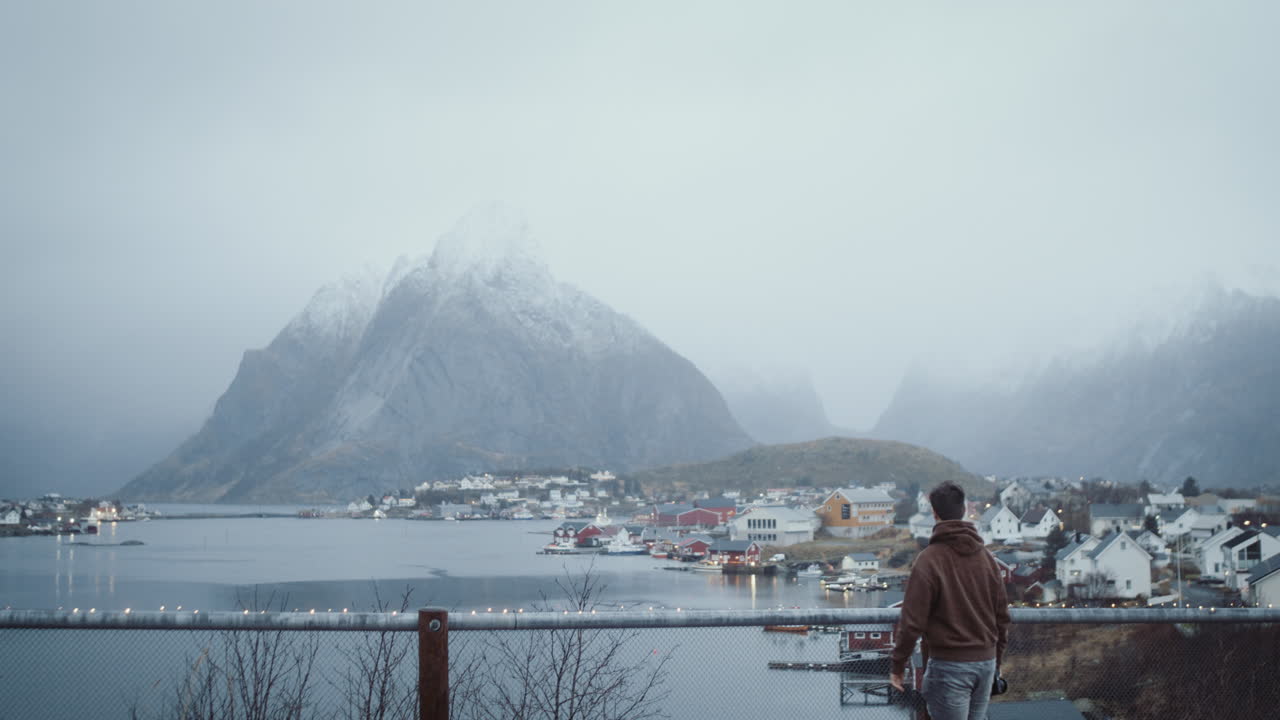 ノルウェーのロフォーテン諸島にある風光明媚なレーヌ村の写真を展望台で撮っている若い男性。