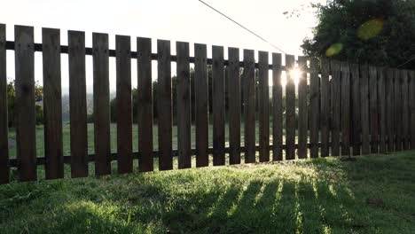 sun shining behind a picket fence over green lawn as camera pans across