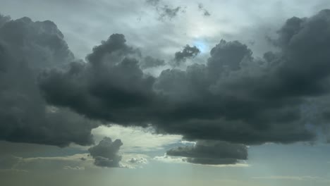 an aerial cloudscape view taken from an airplane cockpit while flying through threattening storm cumulus clouds, with a faded sun hiding behid the clouds. sunset light, backlight.