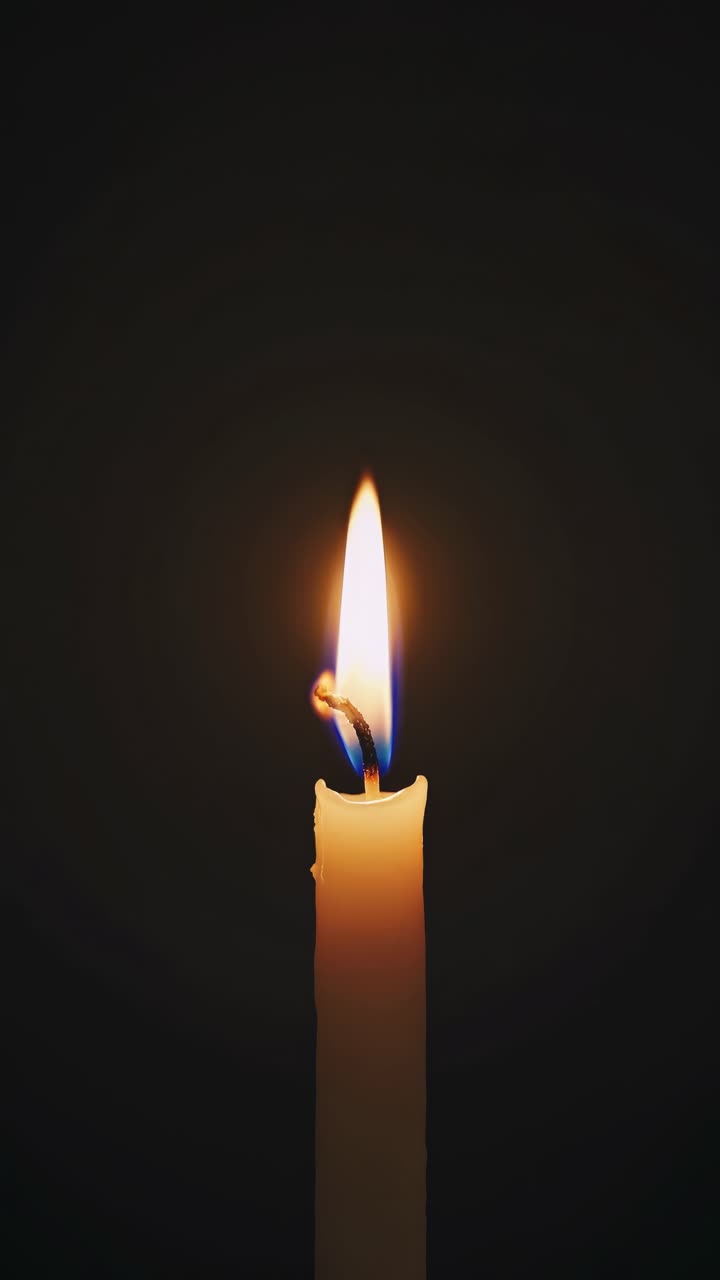 Primo piano della fiamma di una candela singola su uno sfondo scuro, scattata da una angolazione bassa