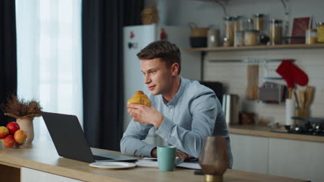 Hombre-Charlando-Reunión-De-Zoom-Con-Amigos-Sentados-En-La-Cocina-Comiendo-Croissant.