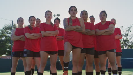 portrait of determined female soccer team with ball on training ground against flaring sun