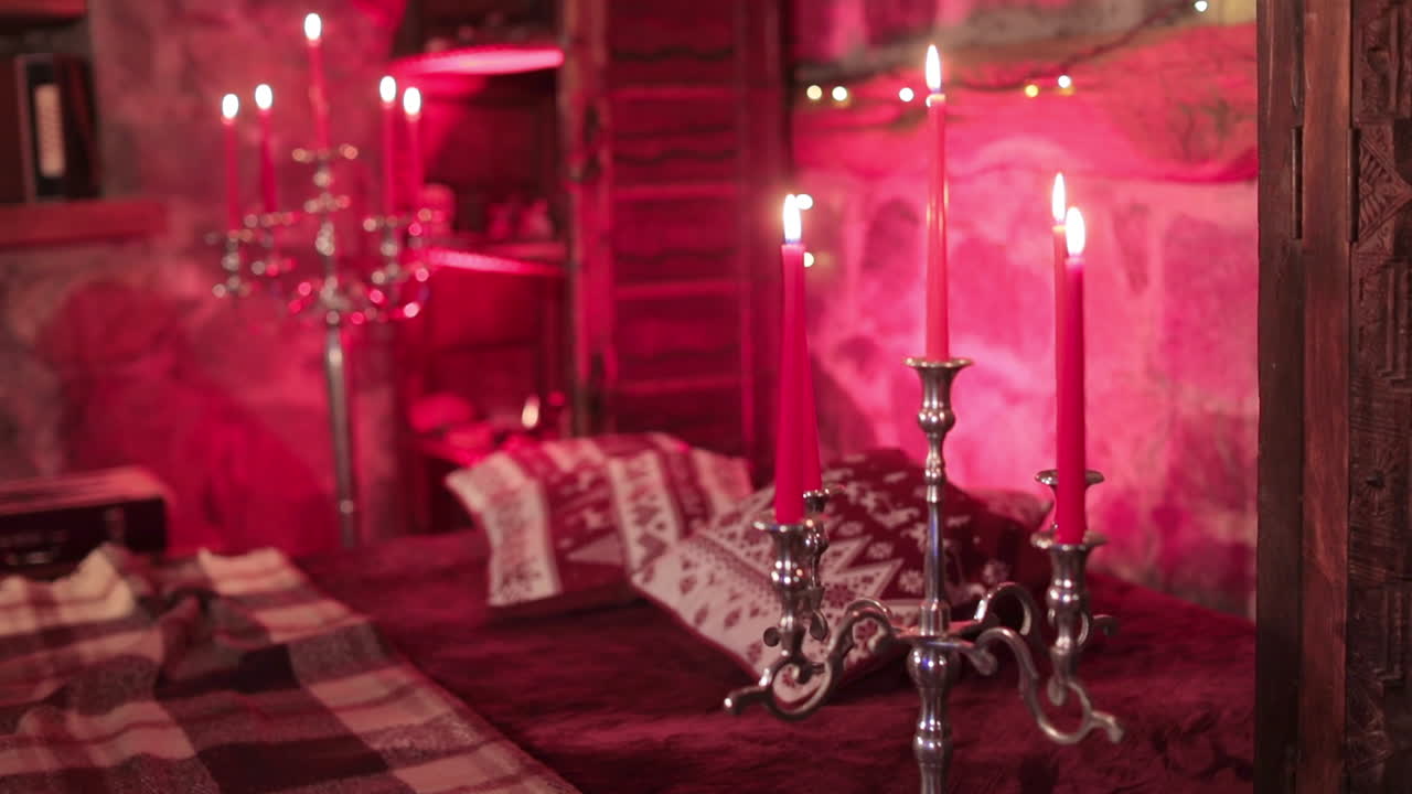 Burning red candles on the high silver candlesticks. Beautiful old-fashioned bedroom with stone walls and red light.