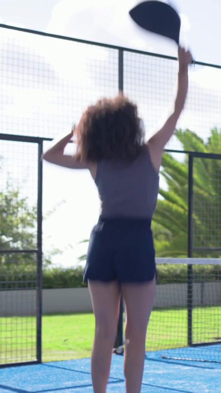 Vertical video: Woman paddle player trying to return low shot, crouching and swinging on blue court