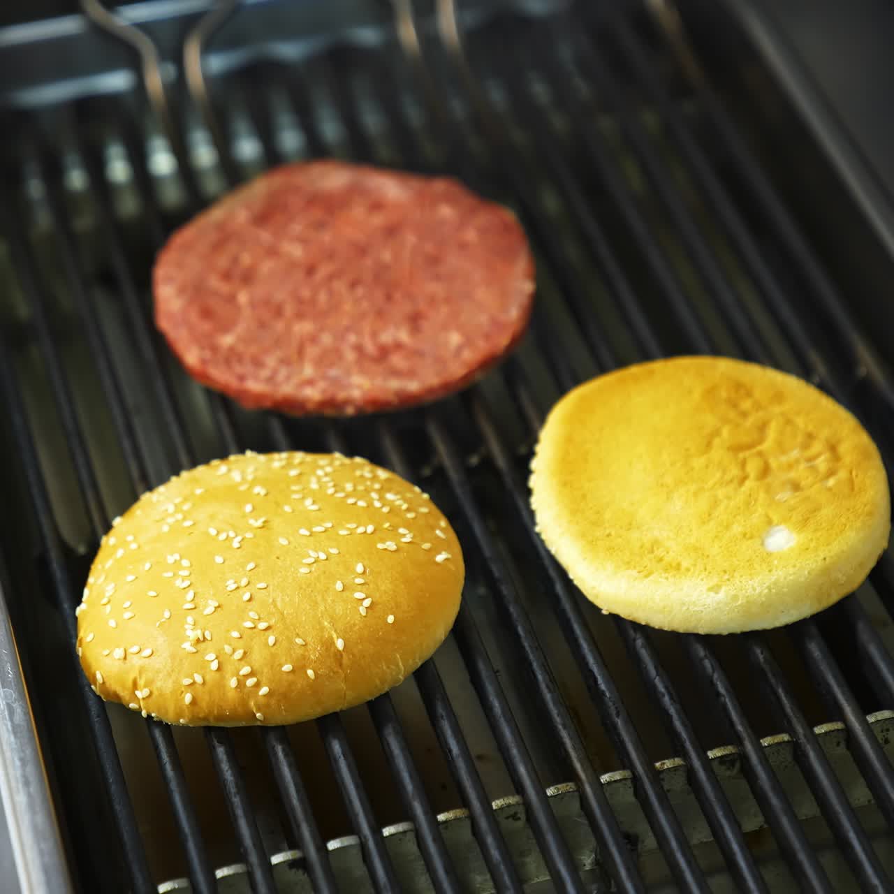 Two burger buns and one cutlet are being cooked on a barbecue grill. Delicious homemade burger