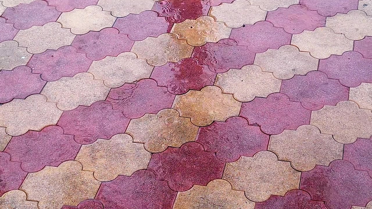 Il pavimento bagnato mostra gocce di pioggia che creano increspature e piccole pozzanghere su piastrelle colorate ad incastro, utile per sfondi a tema pioggia, ambiente urbano, acqua e stagionali