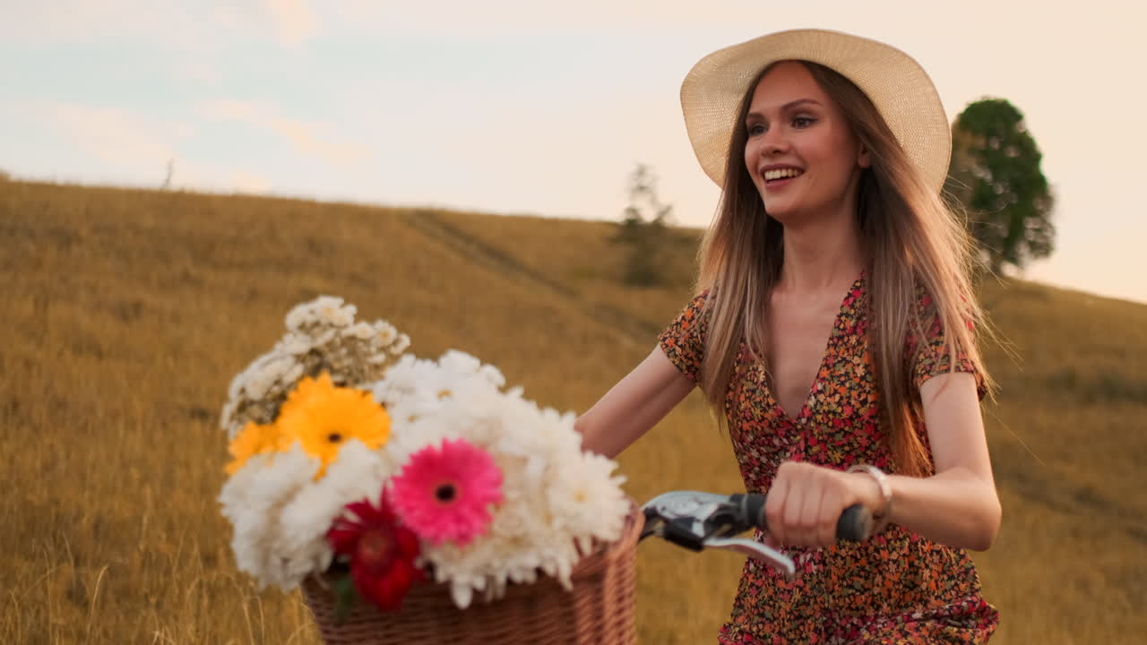 luz de la lente: mujer feliz sonriente en vestido corto está montando una bicicleta con una canasta y flores en el parque con árboles verdes alrededor durante el amanecer. disparo en cámara lenta