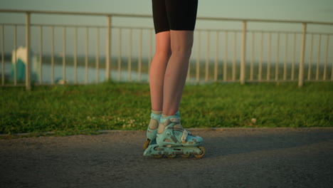 vista de la pierna de una persona patinando hábilmente al aire libre cerca de una barandilla de hierro, con patines deslizándose en el camino y el paisaje urbano borroso en el fondo con vegetación y edificios suavemente iluminados