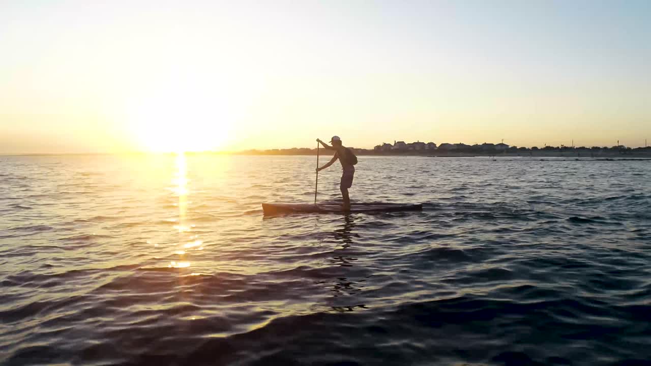 Paddleboarder paddling away into the sunset.