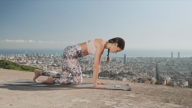 Donna sportiva che guarda una lezione video sullo smartphone durante un allenamento di yoga all'aperto.