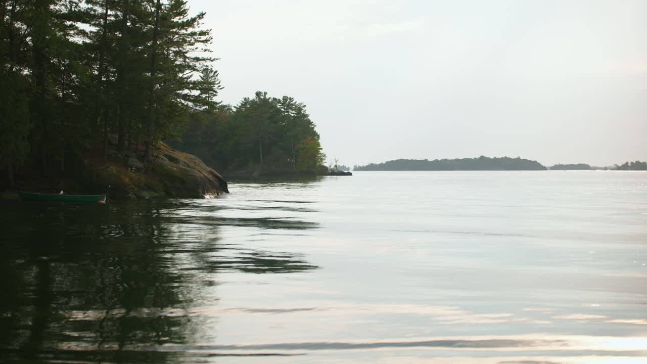 Handheld shot of a tranquil St. Lawrence River scene featuring a canoe by the rocky shoreline of Wellesley Island State Park in Fineview, NY.