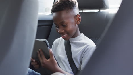 African American boy enjoys a tablet in the backseat of a car