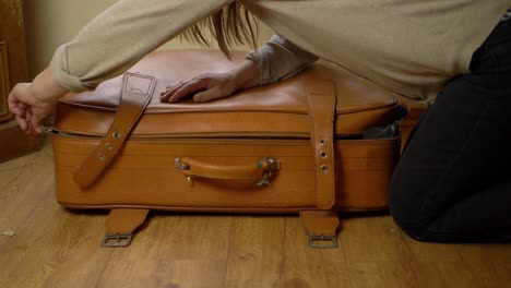 Woman-unzipping-old-brown-suitcase-wide-shot