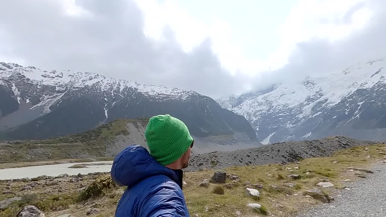 Solo man walking in the Hooker Valley in New Zealand across open expanse towards snow topped mountain peaks (slow motion)