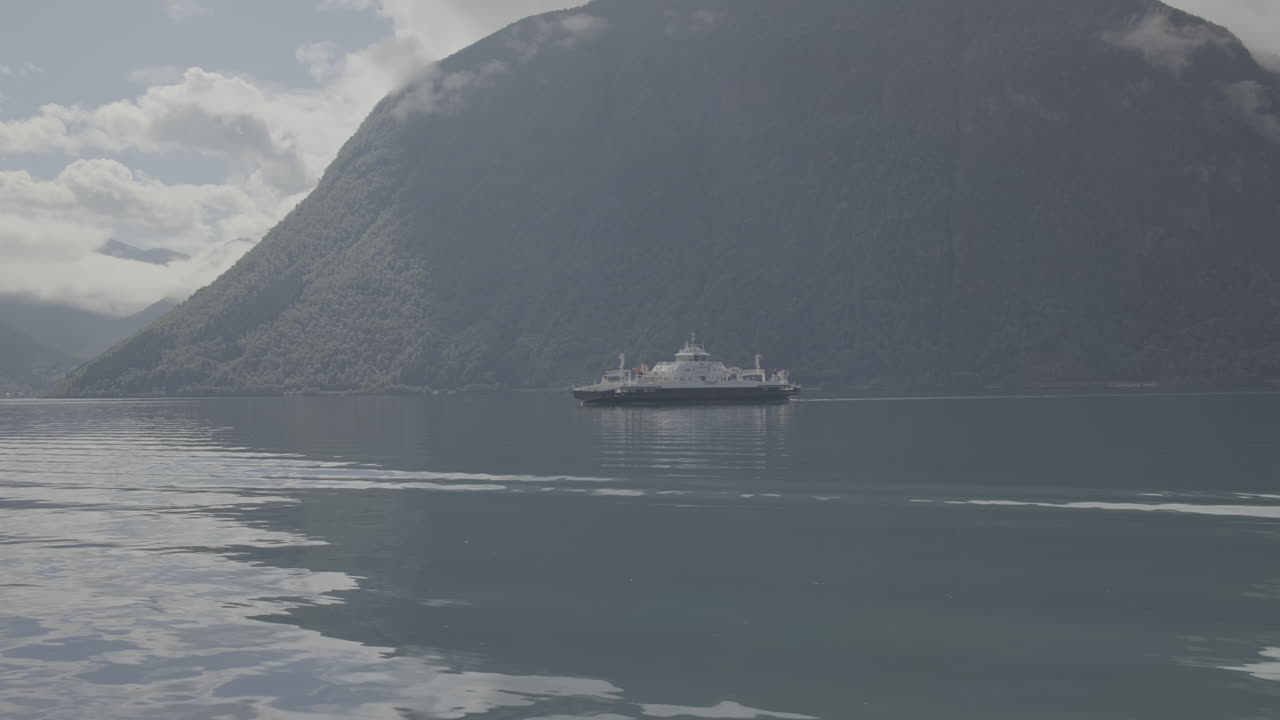 은 날 노르웨이의 피오르드를 가로지르는 자동차 페리, 은 물과 반사, 그리고 배경에 구름과 함께 산.