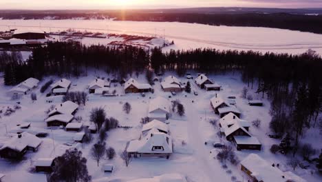 aerial winter sunset over snow-covered neighborhood next to a frozen lake and a forest