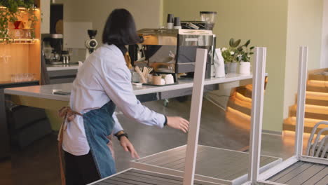 waiter cleaning table in coffee shop, while his female colleague cleaning coffee machine