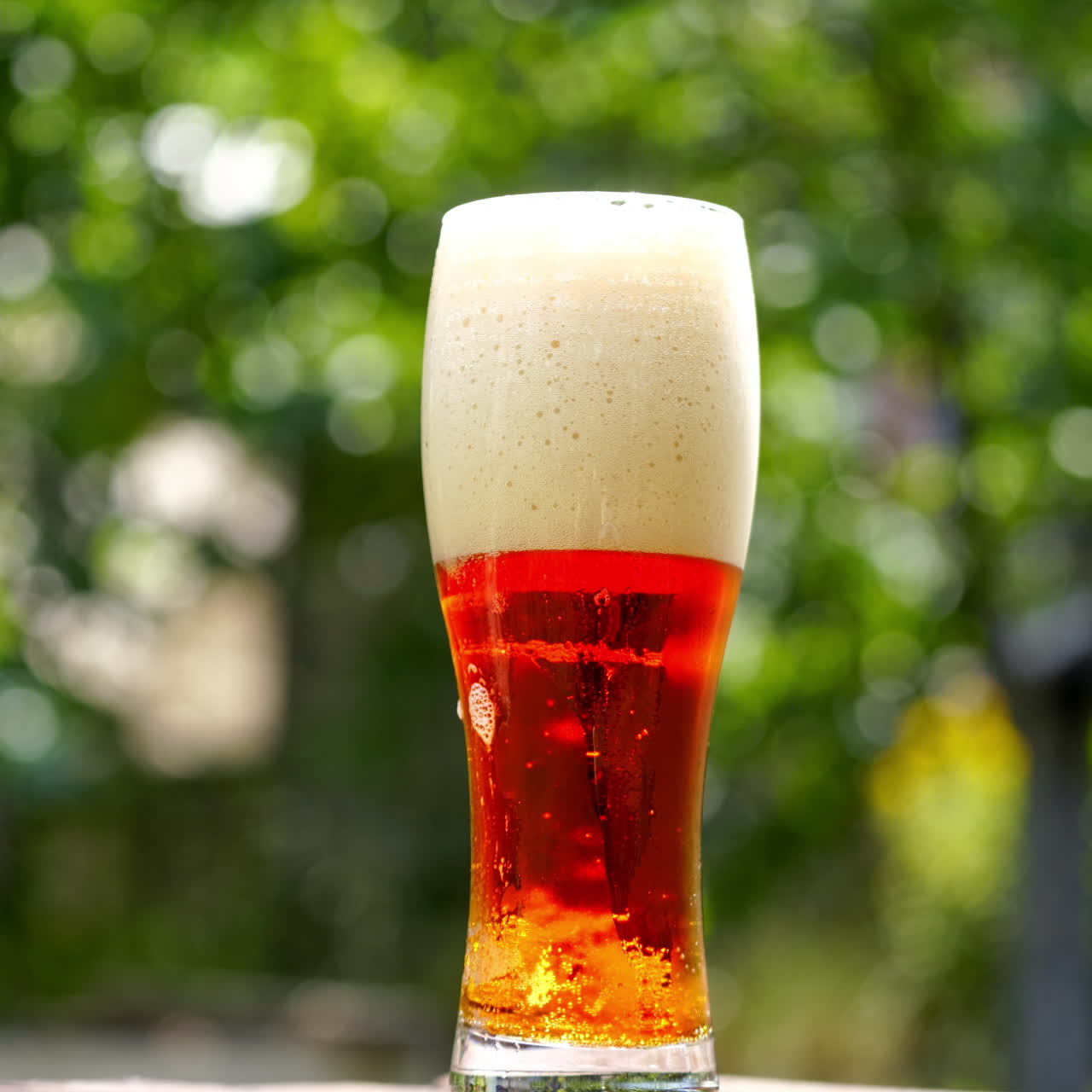 Glass of beer stands on a summer terrace. Full glass of dark beer with foam and small bubbles inside. Close-up.