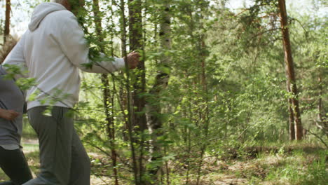 tracking view of senior man and woman jogging along forest trail in morning