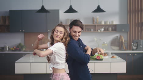 hombre y mujer felices bailando de espaldas a espaldas en la cocina de la casa en cámara lenta.