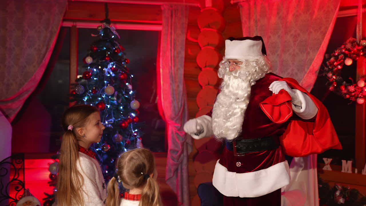 Ho ho ho, Merry Christmas. Two inquisitive girls standing at the evening dark room and listening Santa Clause. Man holding bag with presents. Holiday concept