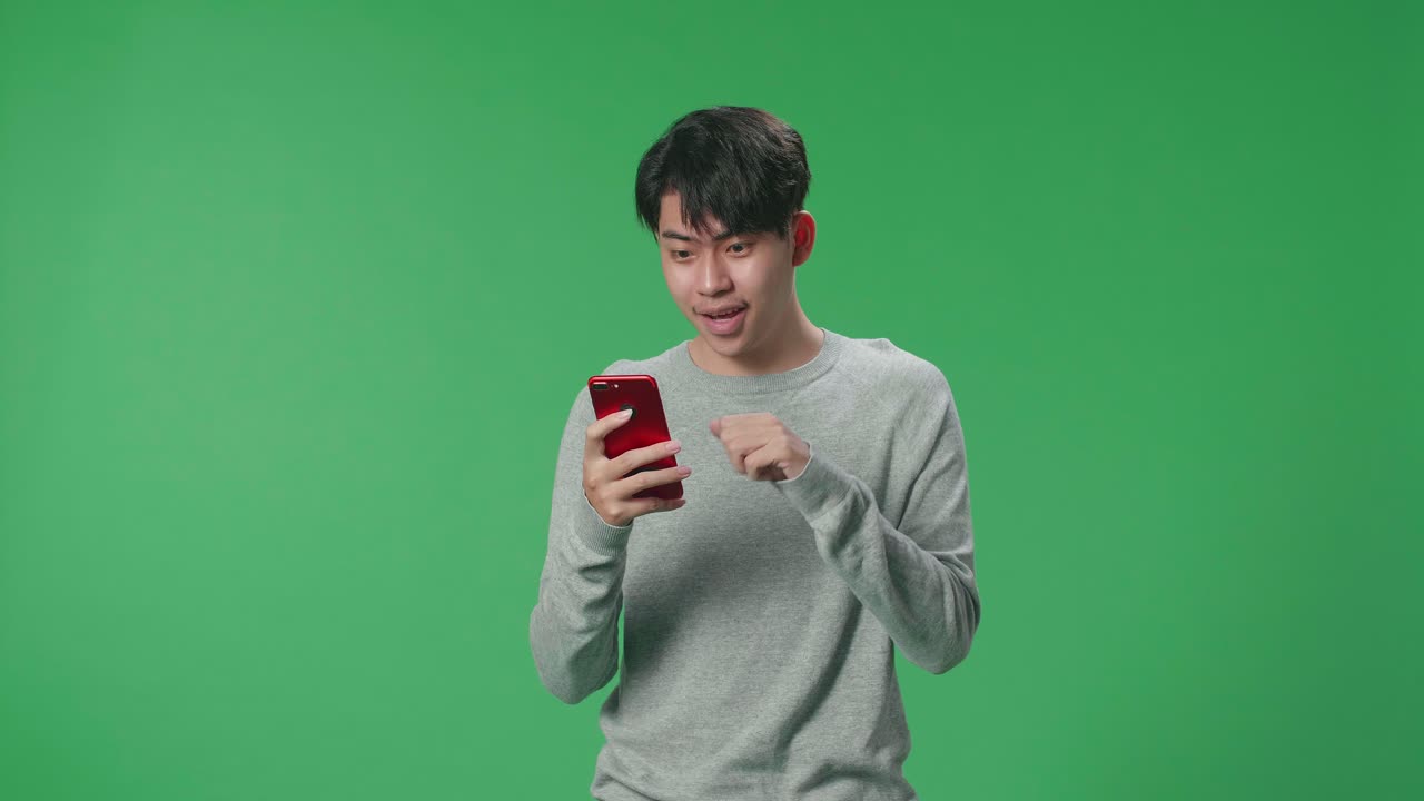 An Asian Man Celebrating While Using Mobile Phone In The Green Screen Studio
