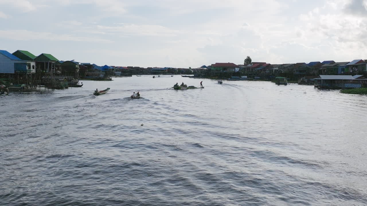 Boat speeds through Tonlé Sap channel lined with colorful stilt houses under bright sky
