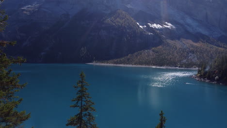 Fantastische-Luftaufnahme-über-Den-Oeschinensee-Und-Vorbei-An-Den-Bäumen-Des-Waldes-Und-Den-Bergen,-Die-Ihn-Umgeben,-An-Einem-Sonnigen-Tag-Und-Mit-Blick-Auf-Das-Türkisfarbene-Wasser