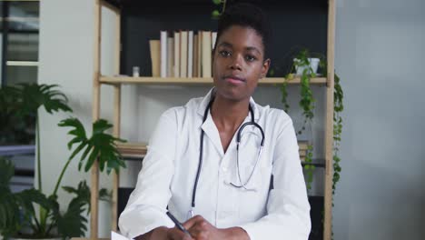 Portrait-of-african-american-female-doctor-having-a-video-chat-listening-and-writing-notes