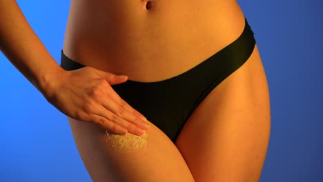 fashionable black bikini on woman with blue background a woman in a stylish black bikini rubs a scrub on her leg against a bright blue background demonstrating elegance and confidence close up