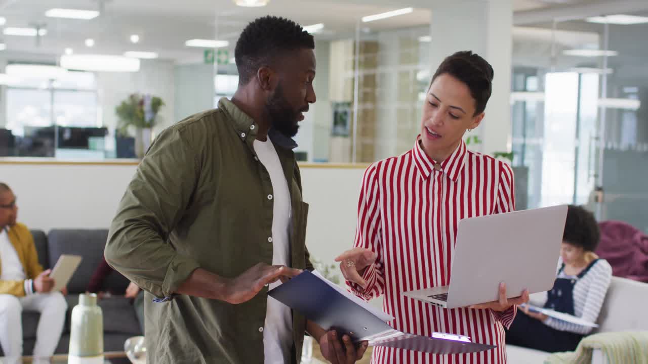 Diverse male and female colleagues using laptop and notebook, having business talk in office